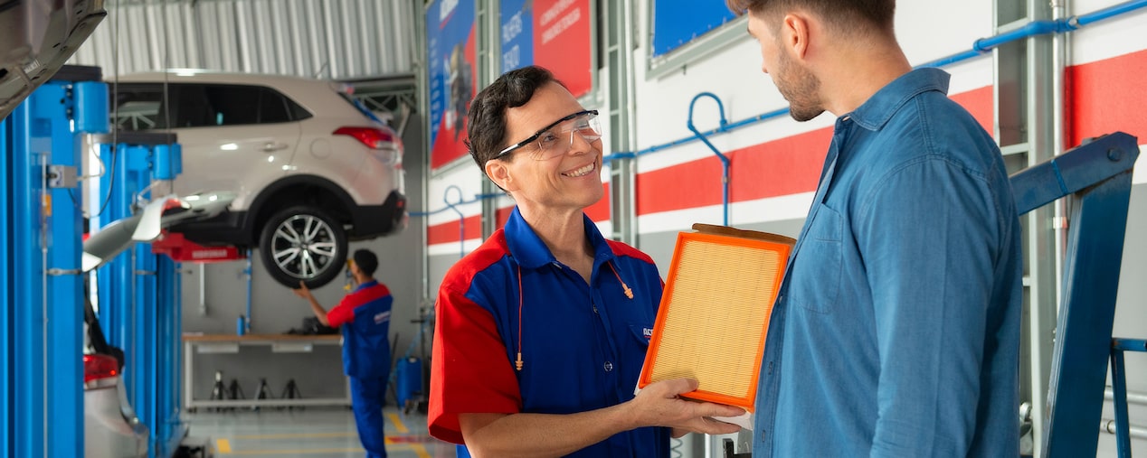Mecánico mostrando filtro de aire ACDelco a cliente en taller automotriz.